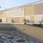 A modern and colorful facade of Mitsui Outlet Park Marine Pia Kobe with wide paved walkways. These pale colors and the "open feeling" inspire the color palette and "Ma" of the Suma area in the kodiad project.