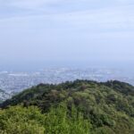 A panoramic view of Kobe city and the sea from the lush green hills of Mt. Rokko under a clear sky.