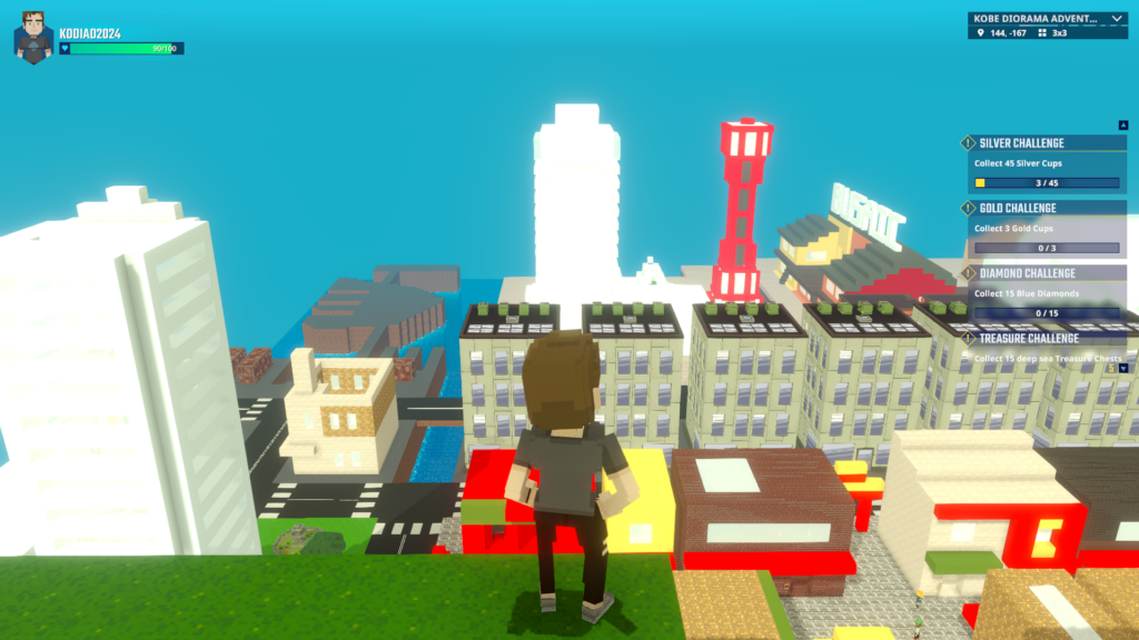 A voxel character standing on the green edge of Mount Rokko in The Sandbox, overlooking the Kobe cityscape including the red Tower and BUSAIC under a clear blue sky.