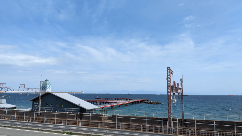 A professional Kobe Guide to Suma Fishing Park, featuring the iconic crimson pier under a blue sky, reflecting the "Architecture of Silence" in Kobe Art.